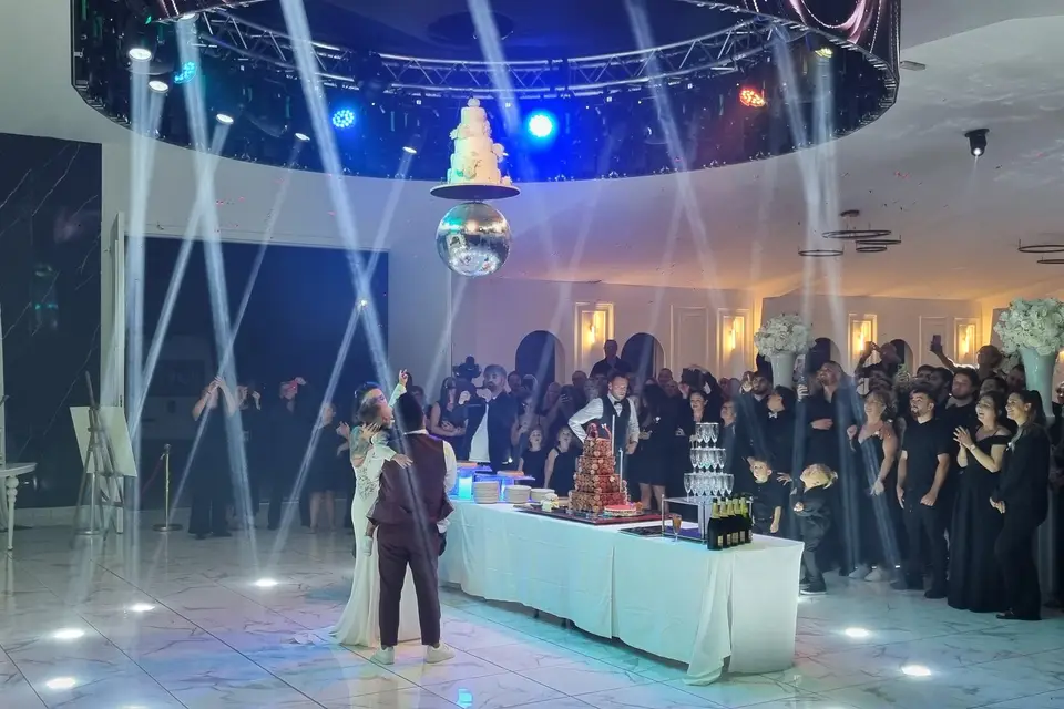 Les mariés sous le gâteau suspendu et la boule à facettes, entourés des invités